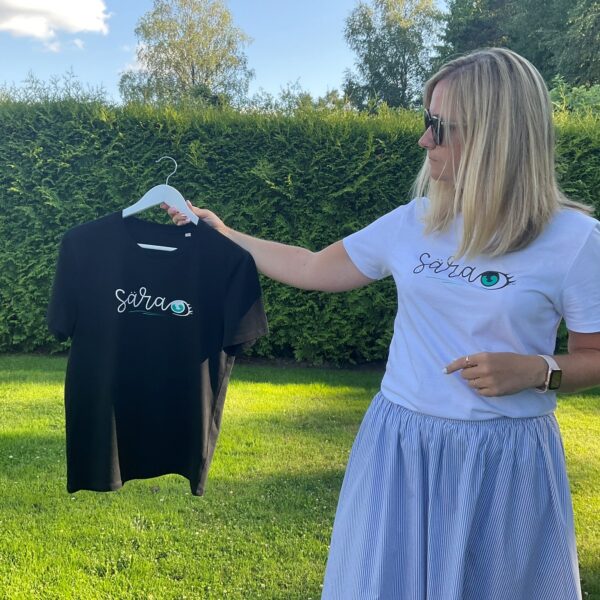 The woman shows the new T-shirt "Särasilm" in black and wears the white T-shirt.